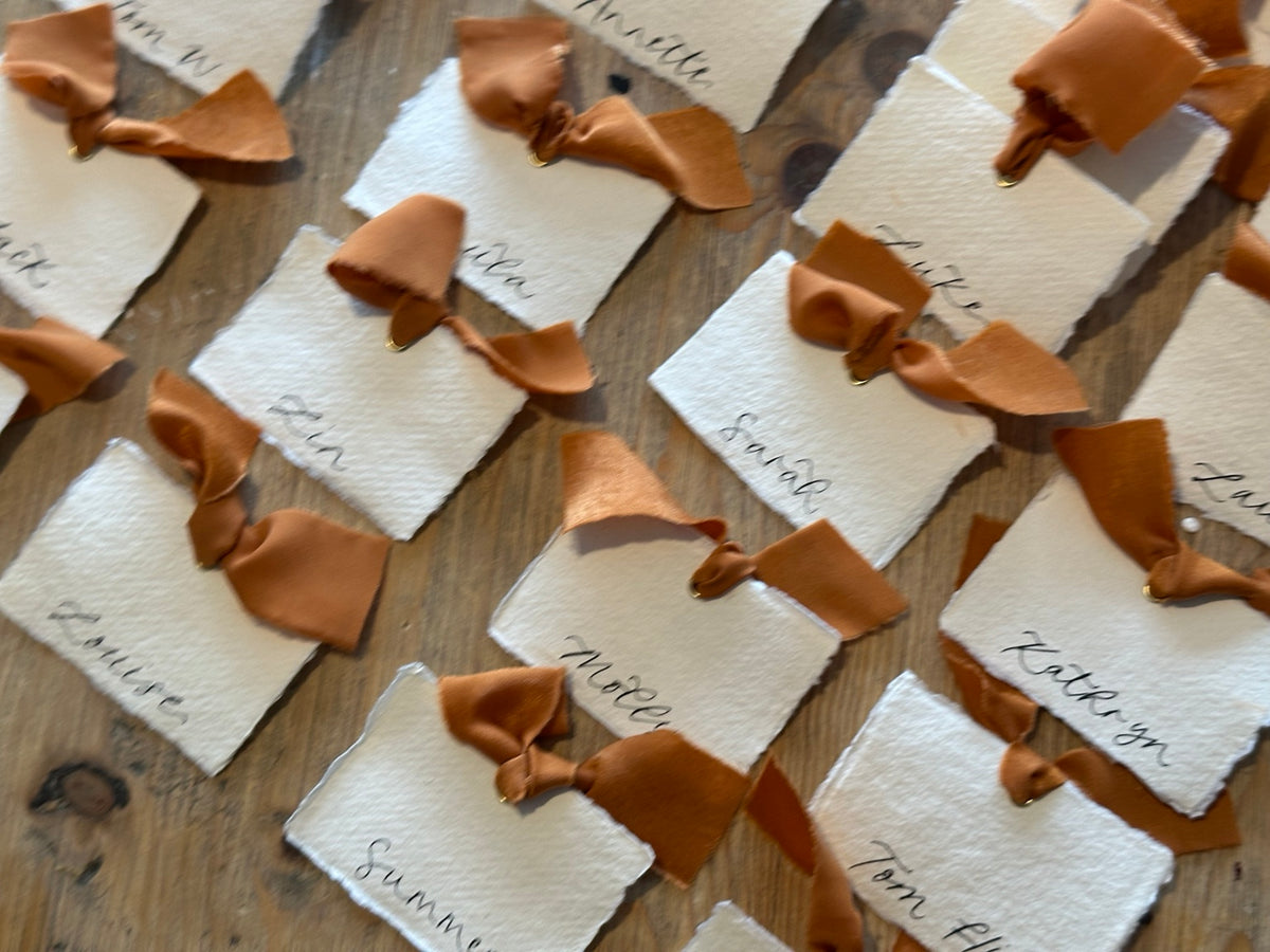 Handmade paper place cards with ochre ribbon and calligraphy, styled overhead view