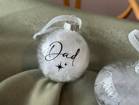 Clear feather ornament with 'Dad' text on a soft surface