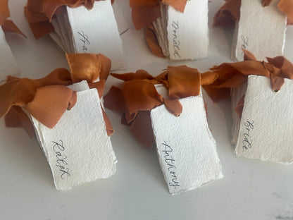 Handmade paper wedding place cards with ochre chiffon ribbon and gold eyelets