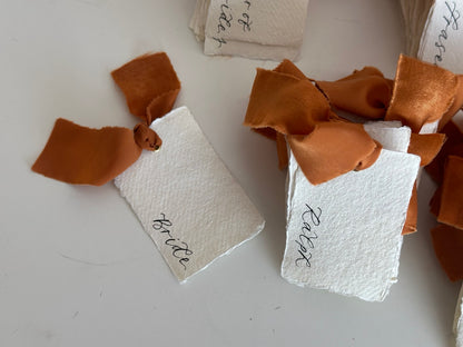 Handmade paper wedding place cards with ochre ribbon and gold eyelets