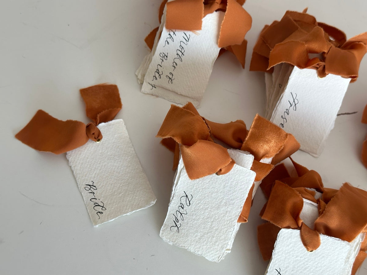 Ochre chiffon ribbon tied through handmade paper wedding place cards
