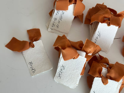 Ochre chiffon ribbon tied through handmade paper wedding place cards