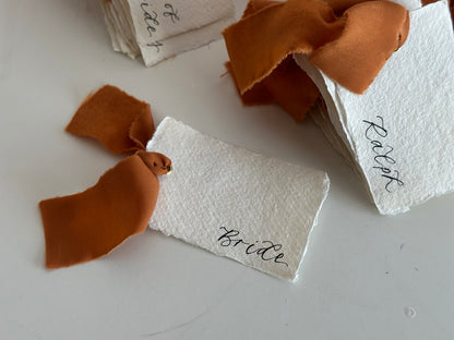 Close-up of handmade paper wedding place cards with ochre chiffon ribbon