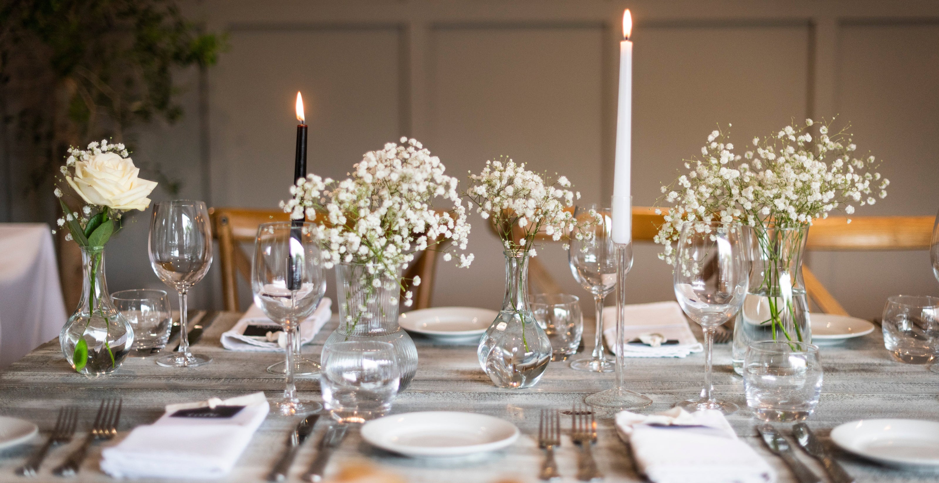 Elegant table setting with flowers, candles, and cutlery on a wooden table.