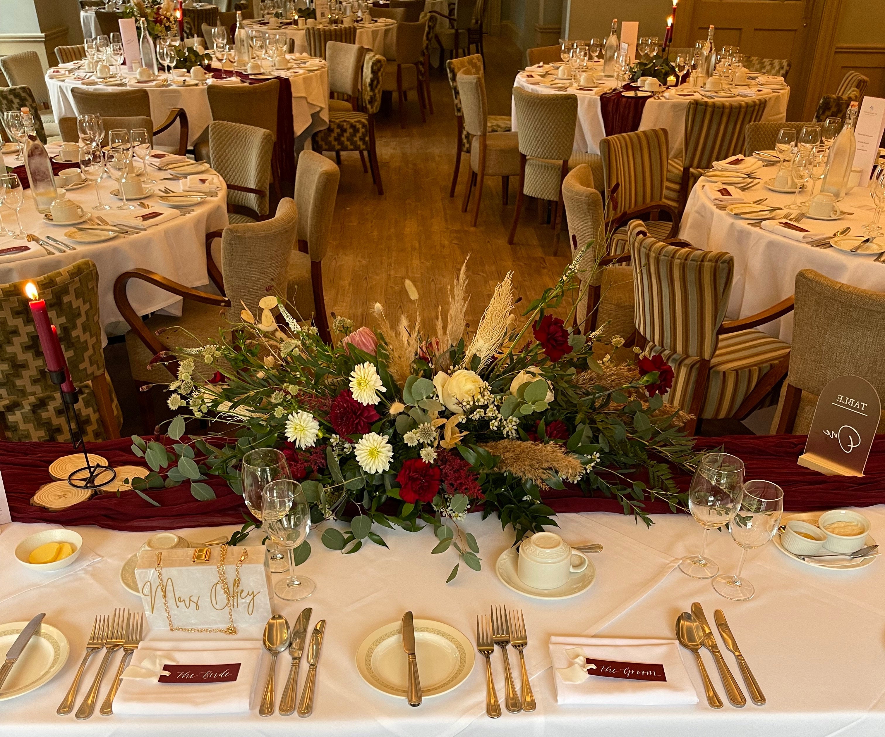 Wedding table setting with floral arrangement and cutlery on a white tablecloth with burgundy and white calligraphy place cards