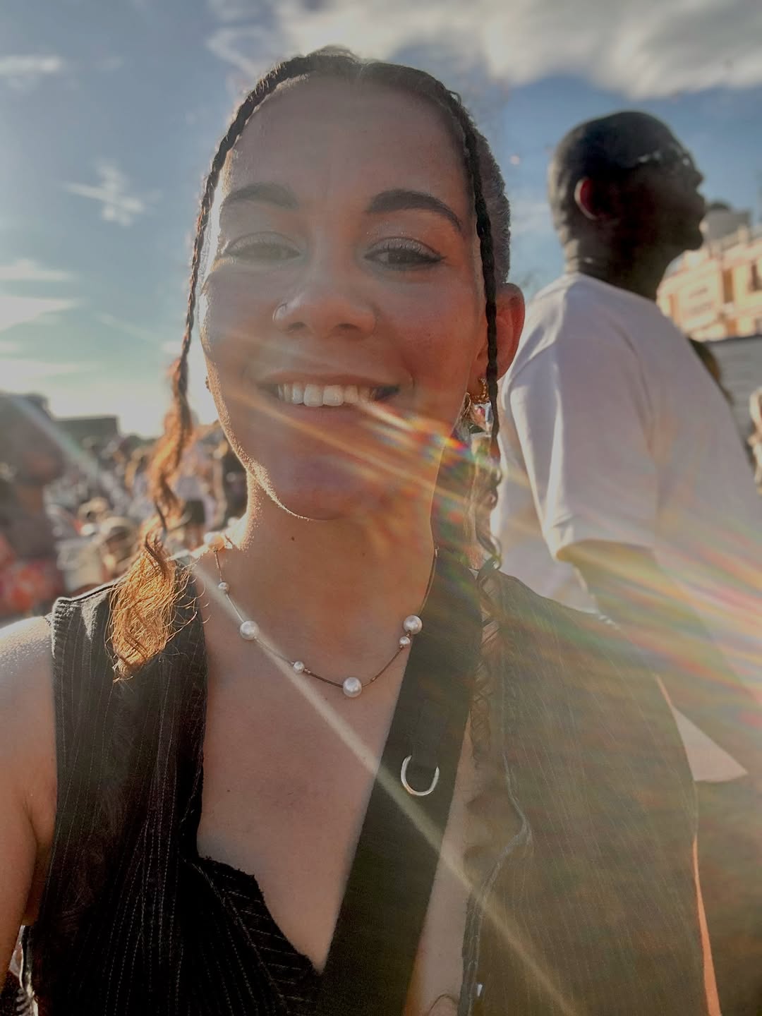 Woman with braided hair smiling outdoors with a lens flare effect