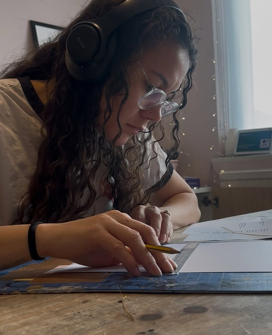 calligrapher sitting at a desk with headphones on writing wedding stationery on paper.