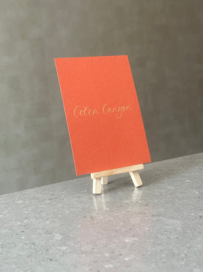 Orange wedding table name sign with gold handwritten calligraphy on wooden easel