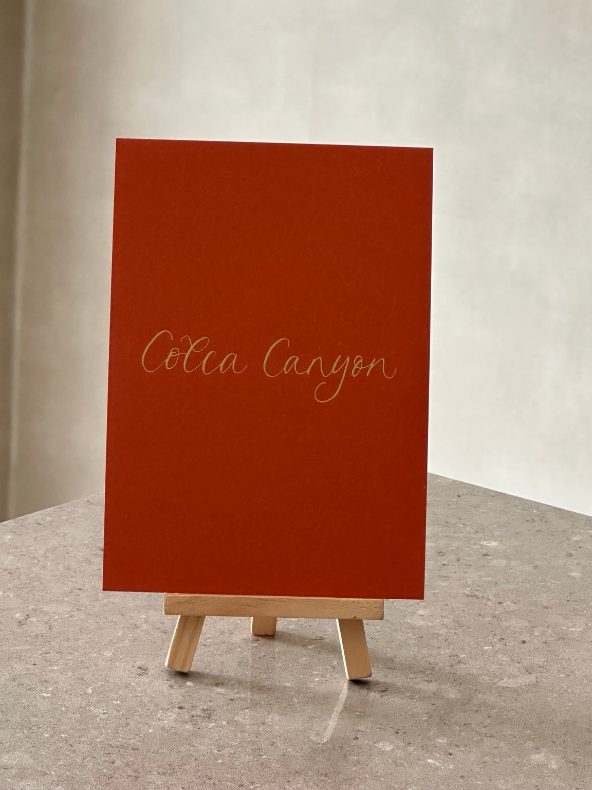 Orange wedding table name sign with gold handwritten calligraphy on wooden easel