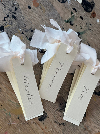 Ivory calligraphy wedding place card with champagne ribbon, silver ink and silver eyelet