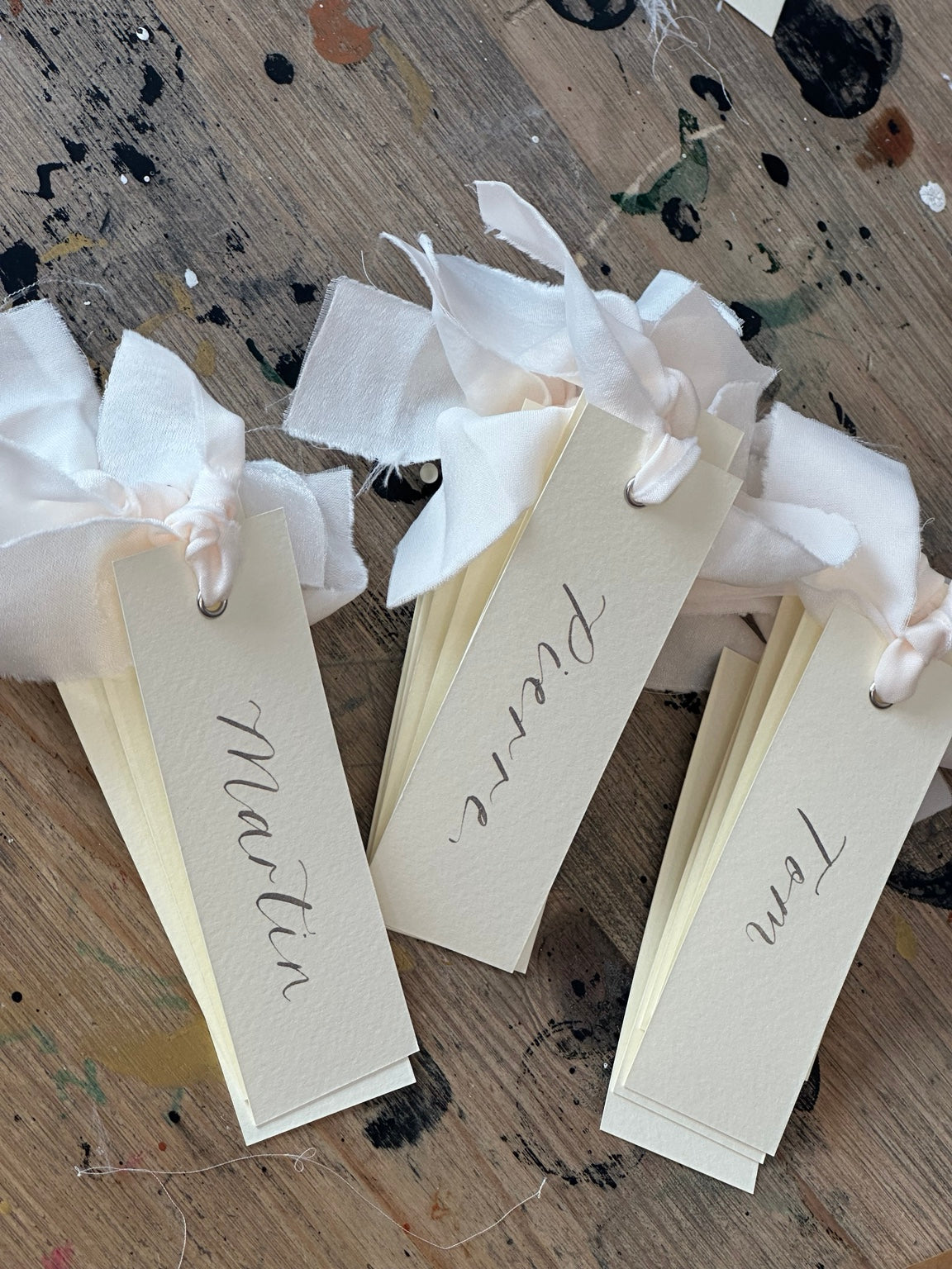 Ivory calligraphy wedding place card with champagne ribbon, silver ink and silver eyelet