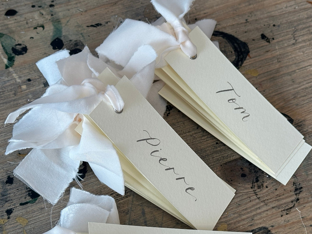 Ivory calligraphy wedding place card with champagne ribbon, silver ink and silver eyelet