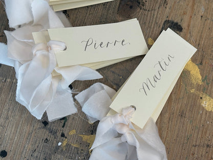 Ivory calligraphy wedding place card with champagne ribbon, silver ink and silver eyelet