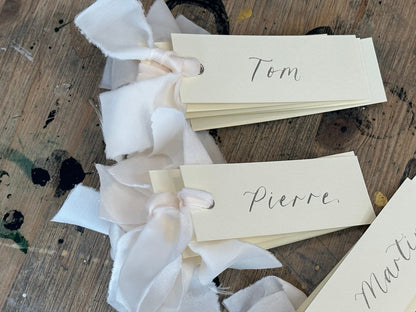 Ivory calligraphy wedding place card with champagne ribbon, silver ink and silver eyelet