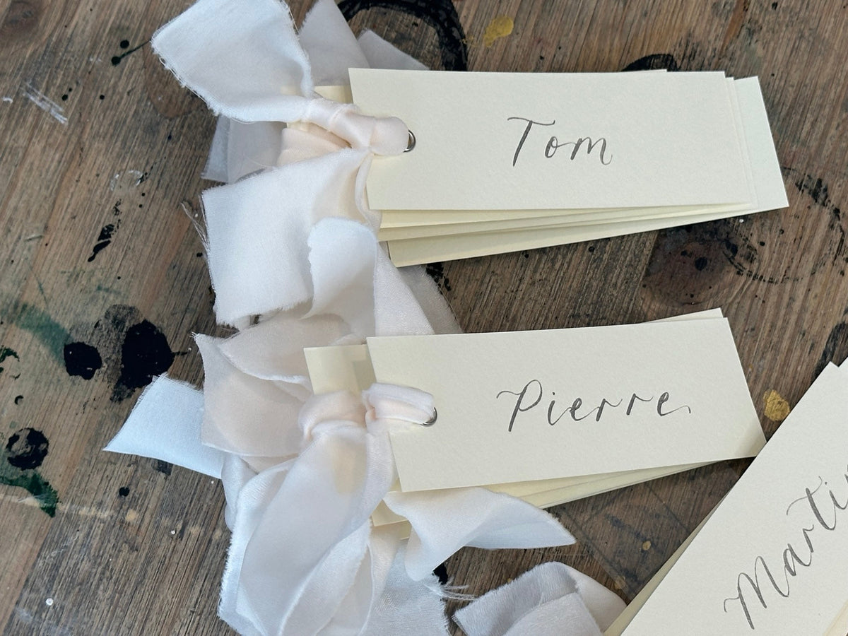 Ivory calligraphy wedding place card with champagne ribbon, silver ink and silver eyelet