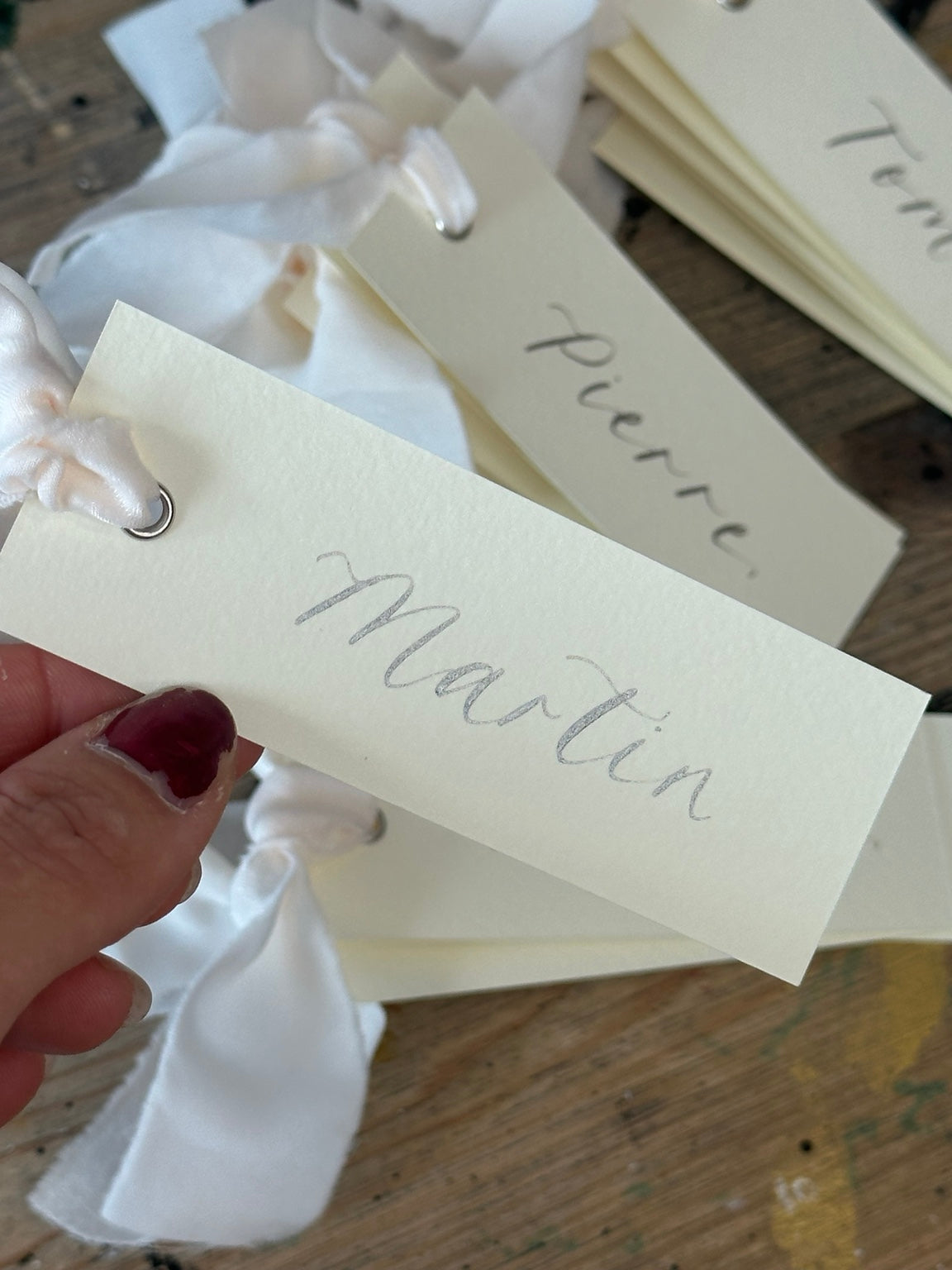 Ivory calligraphy wedding place card with champagne ribbon, silver ink and silver eyelet
