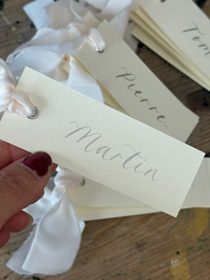 Ivory calligraphy wedding place card with champagne ribbon, silver ink and silver eyelet
