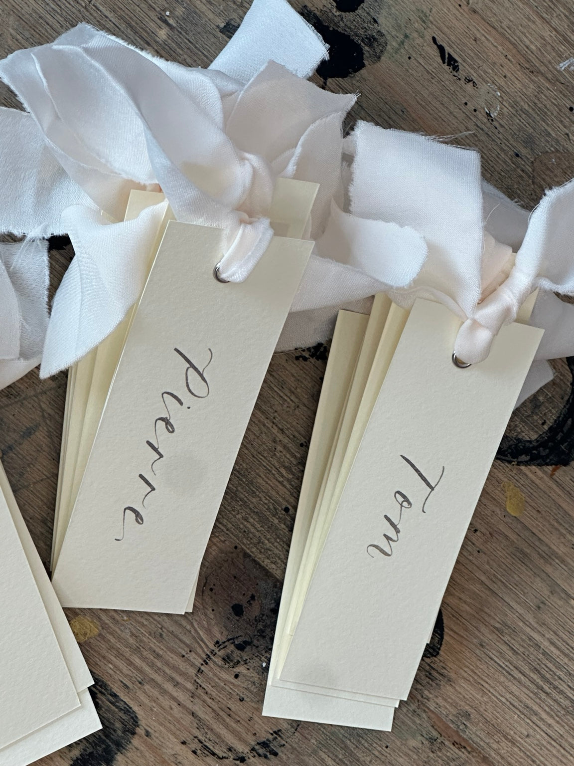 Ivory calligraphy wedding place card with champagne ribbon, silver ink and silver eyelet