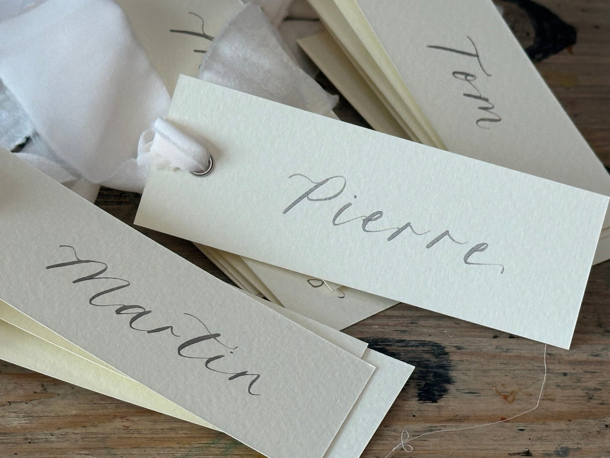 Ivory calligraphy wedding place card with champagne ribbon, silver ink and silver eyelet