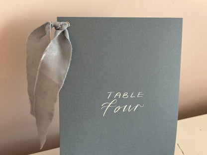 Mixed lettering wedding table number sign on dusky blue card with chiffon ribbon and silver calligraphy