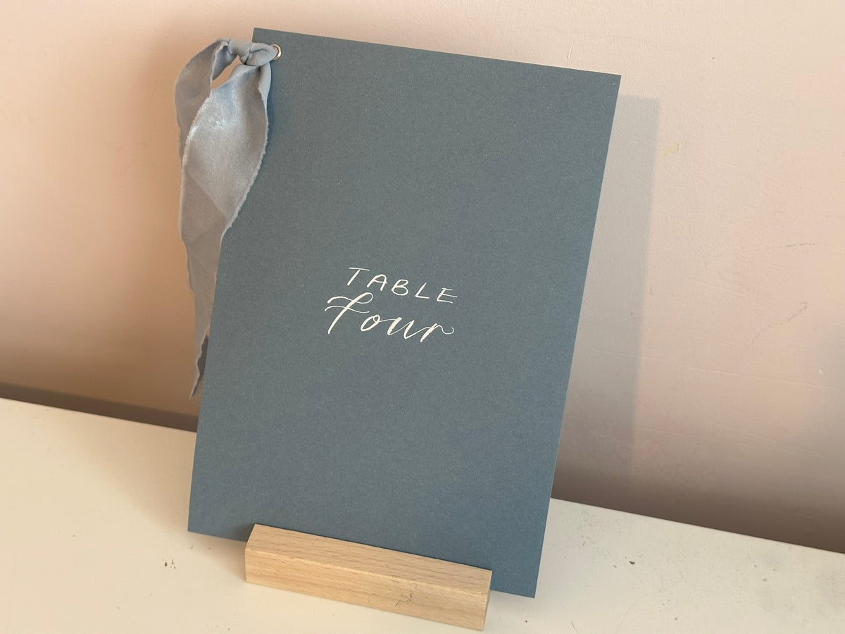 Mixed lettering wedding table number sign on dusky blue card with chiffon ribbon and silver calligraphy