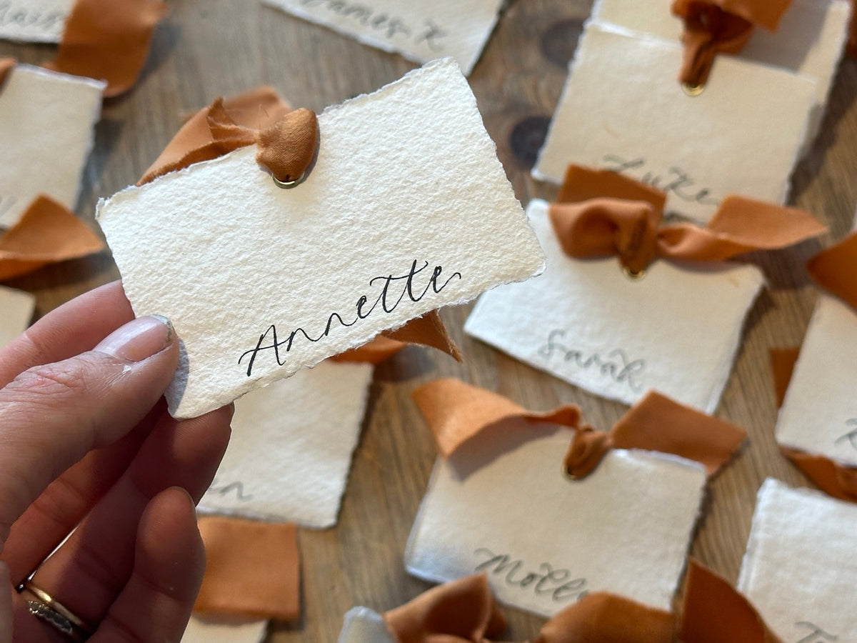 Handwritten handmade paper place card with ochre ribbon and gold eyelet, close-up