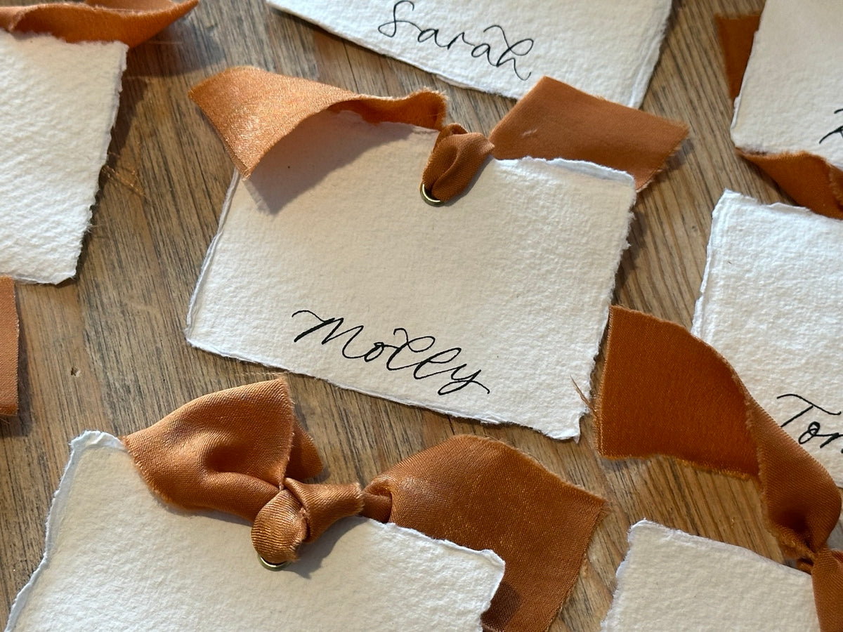 Handmade paper place card with ochre ribbon and handwritten name, close-up