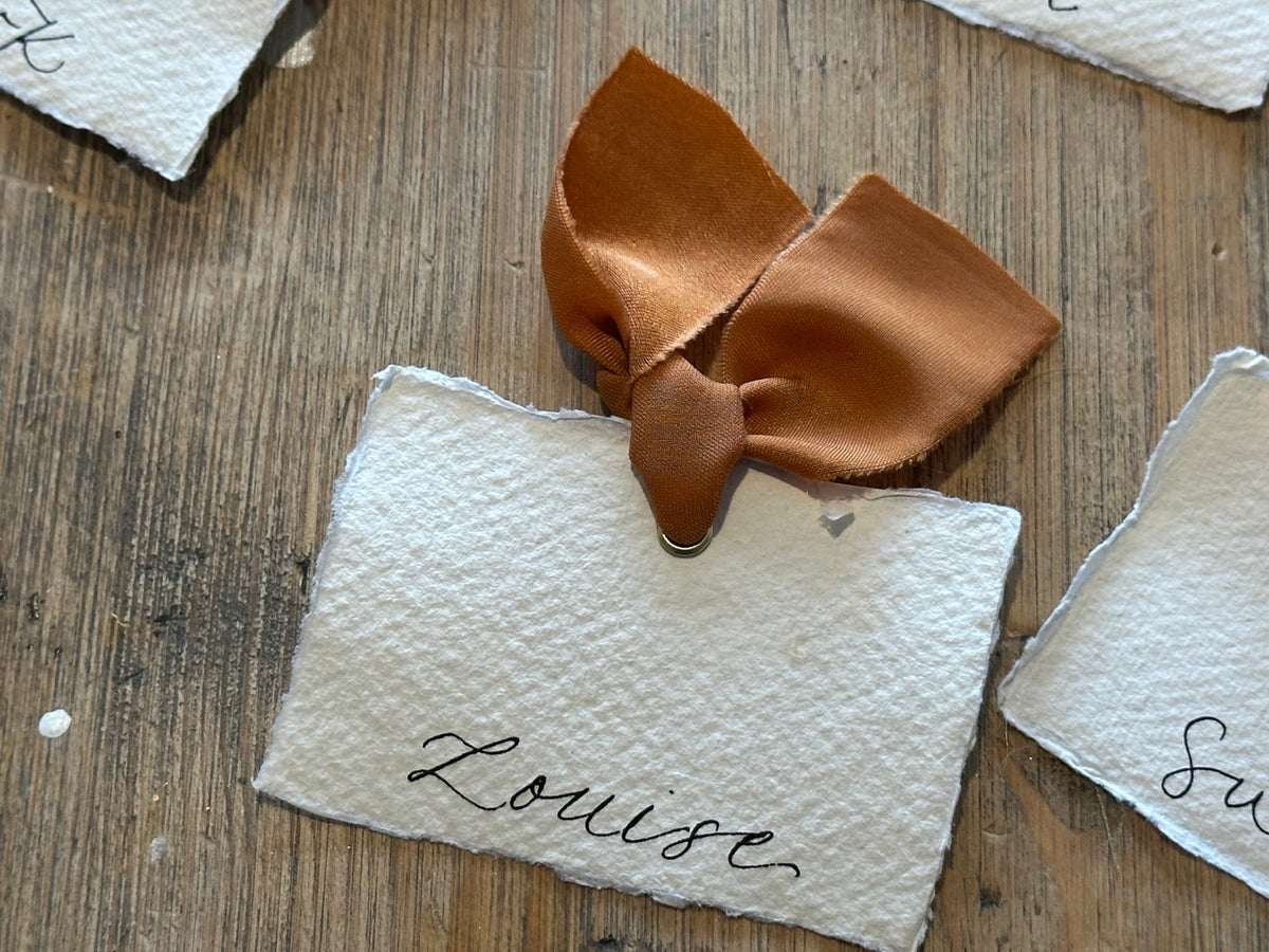 Handmade paper place cards with ochre ribbon and calligraphy, detail view