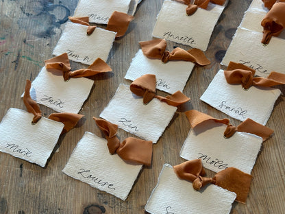 Handmade cotton rag place cards with ochre ribbon and handwritten names, table arrangement