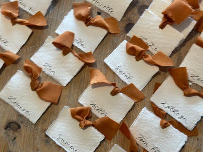Handmade paper place cards with ochre ribbon and calligraphy, styled overhead view