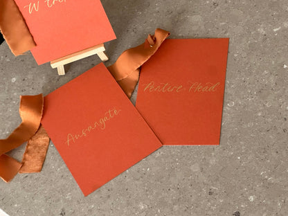 Ochre ribbon wedding table name cards with handwritten gold calligraphy