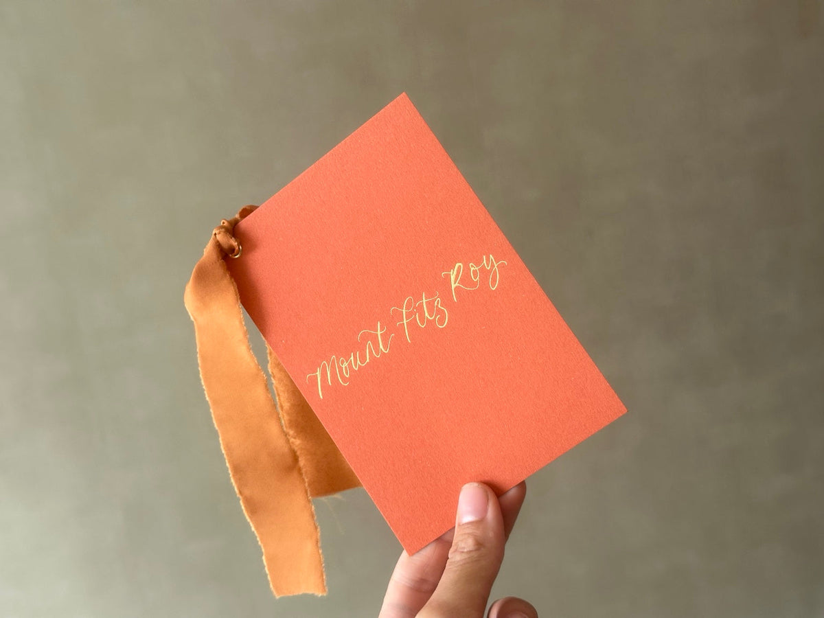 Handheld ochre calligraphy wedding table name card with ribbon