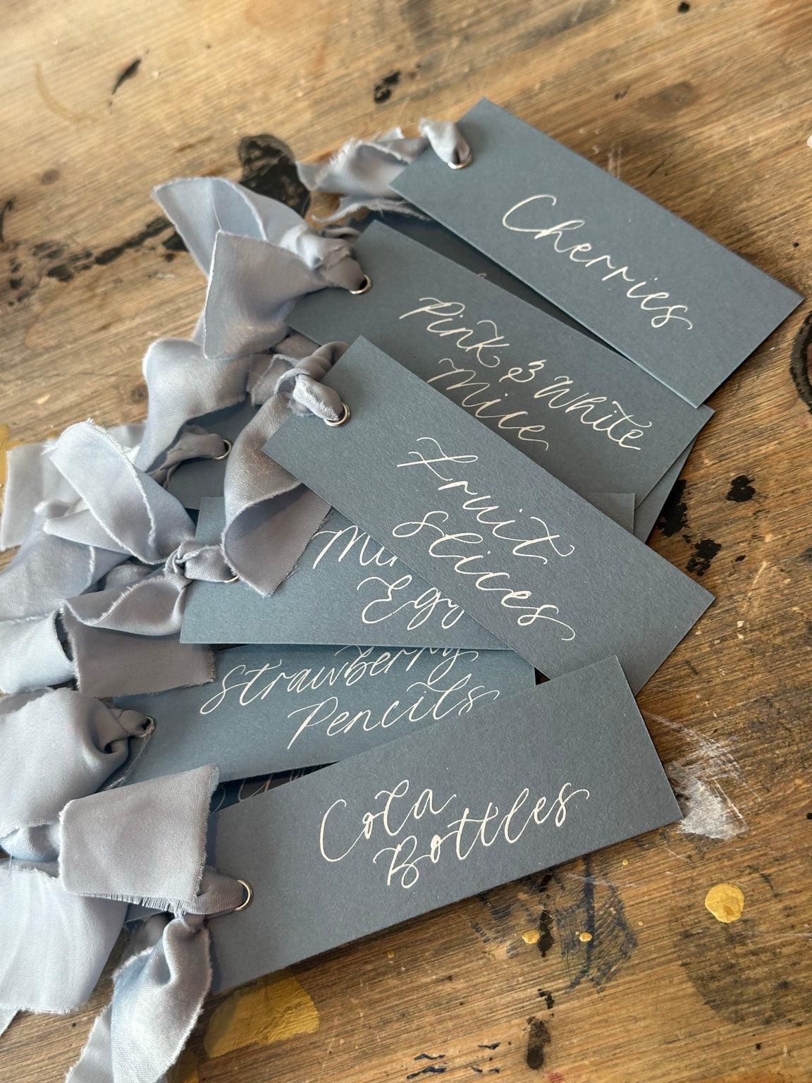Dusky blue wedding sweet cart food tags with white handwritten calligraphy and silver eyelets