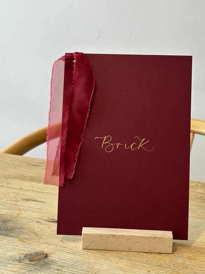 Burgundy wedding table name sign with gold calligraphy and wine ribbon