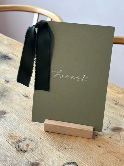 Forest green wedding table name sign with white calligraphy and dark ribbon