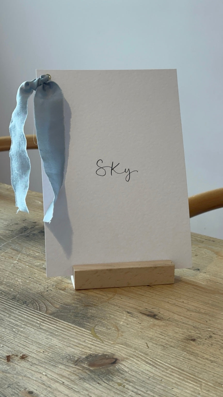 Ivory wedding table name sign with dusky blue ribbon and black calligraphy